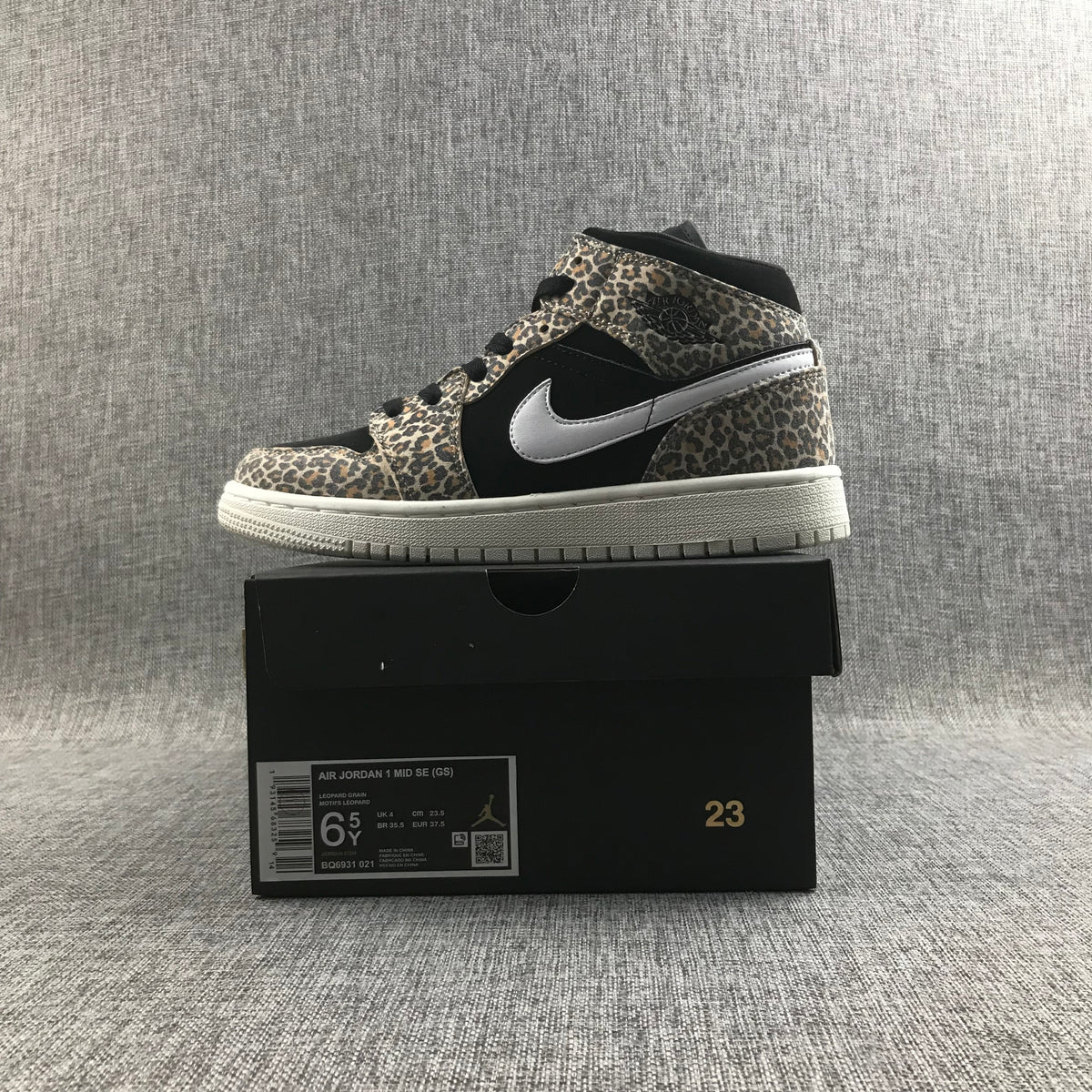 Side view of the sneaker displayed on a black box; the label shows Air Jordan 1 Mid SE (GS), style BQ6931-021, EU 37.5, and 23.5 cm.