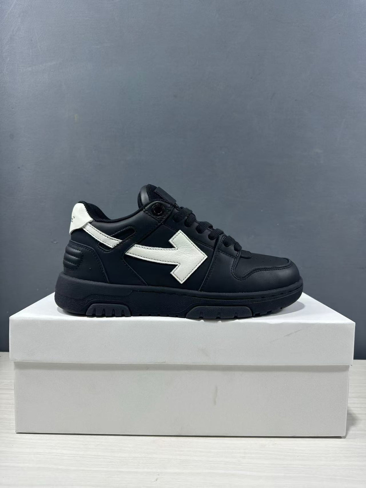 Single side profile of the black and white sneaker showing its low-top silhouette, white arrow detail, and textured outsole.