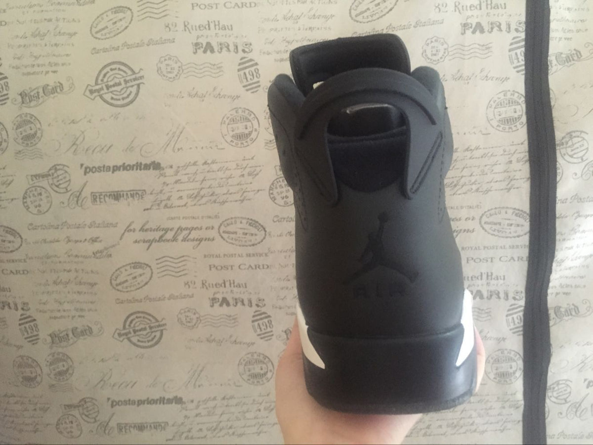 Close rear view of a black high-top sneaker showing the heel pull tab, branding, and white outsole accents.
