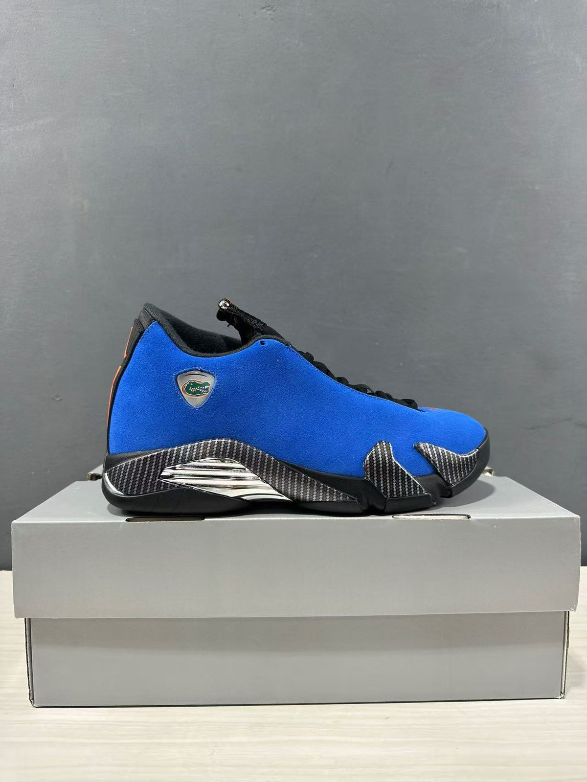 Side profile of a blue and black Jordan Air Jordan 14 Retro sneaker displayed on a box.