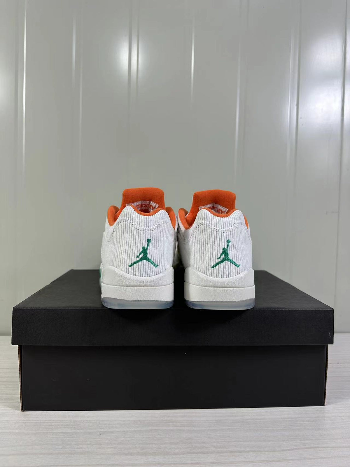 Rear view of the pair with green Jumpman logos on the white heel panels and orange collar lining.