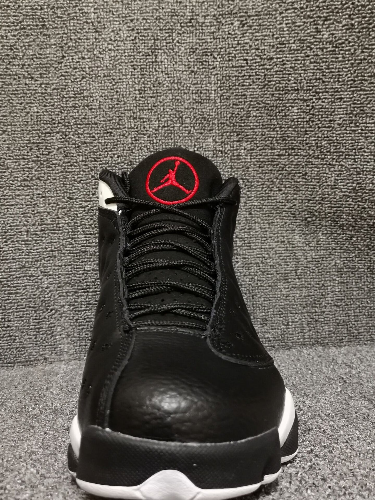 Front view of black high-top sneakers with red tongue emblem and white outsole accents