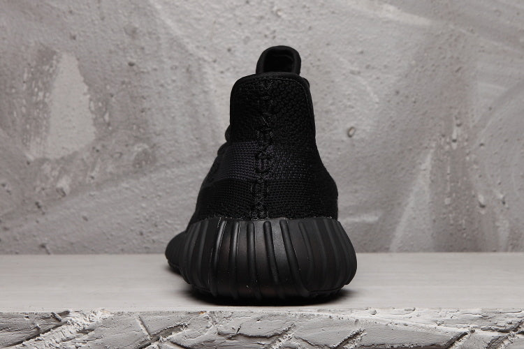 Rear view of a black Yeezy 350 V2 sneaker showing the heel construction and ribbed outsole.