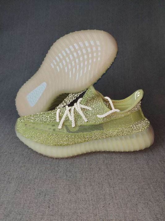 Green Yeezy 350 V2-style sneaker shown from the side with a light cream sole and a second shoe lifted behind it.