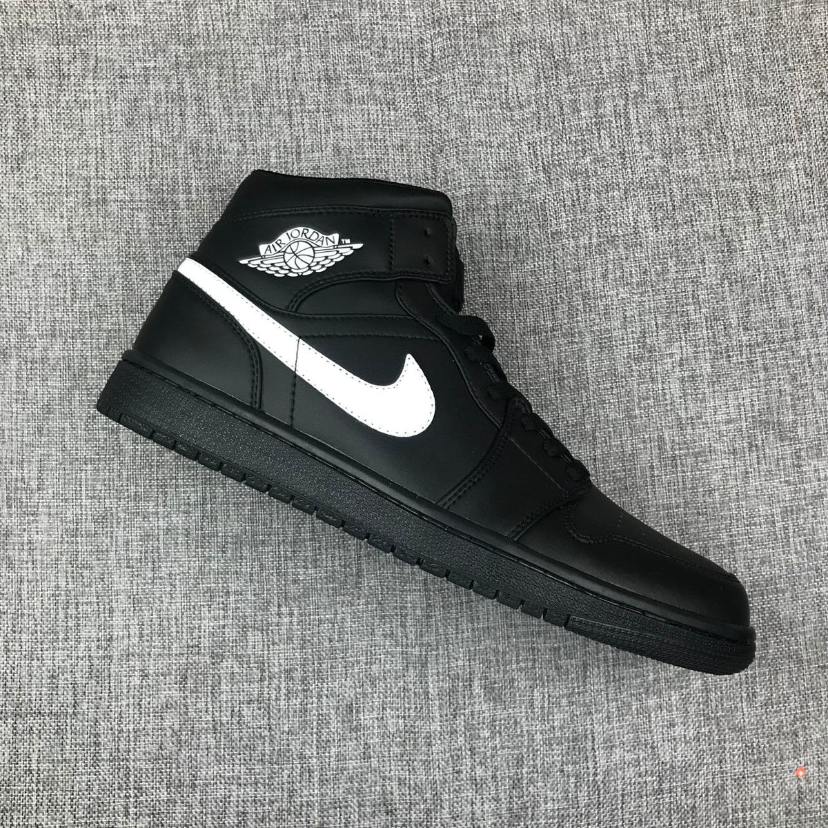 Angled top-side view of a black and white mid-top sneaker with visible collar branding.