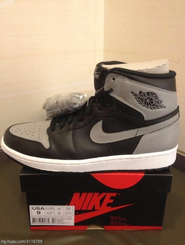 Black and grey Jordan 1 high-top sneaker shown on a Nike shoebox, with the box label visible.