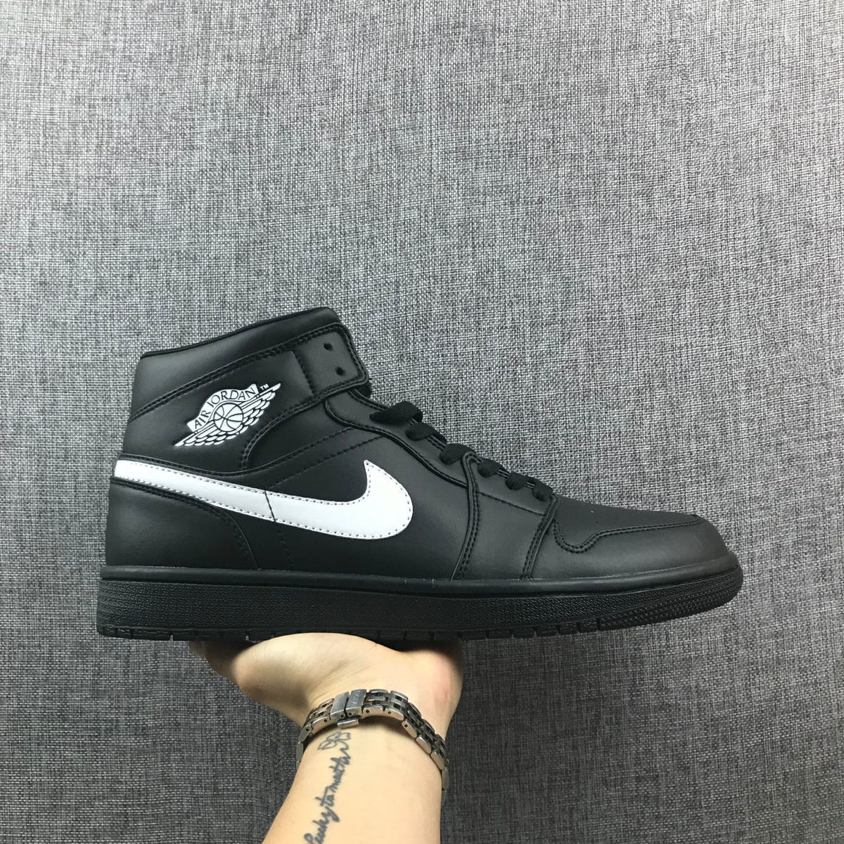 Side profile of a black and white Jordan mid-top sneaker showing the white Swoosh and winged collar logo.