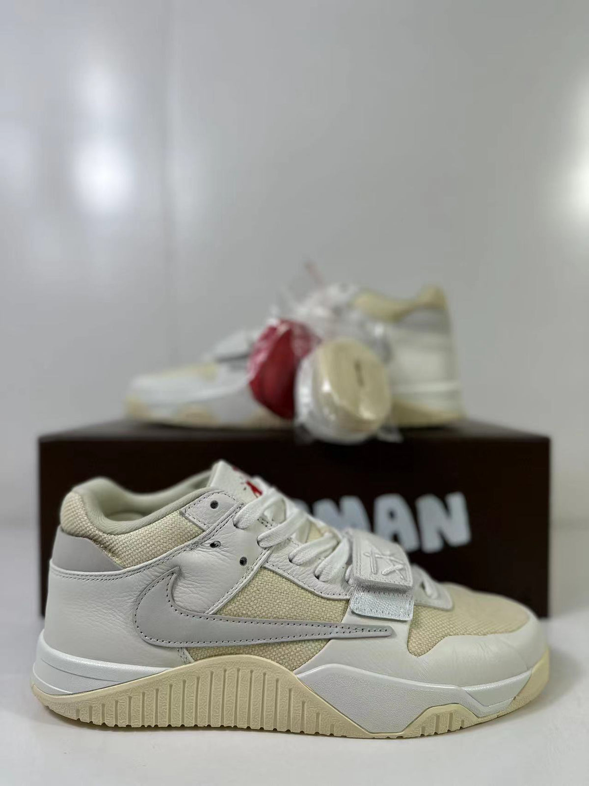 Three-quarter product view showing the cream and white upper, red spare laces, and gray heel detailing.