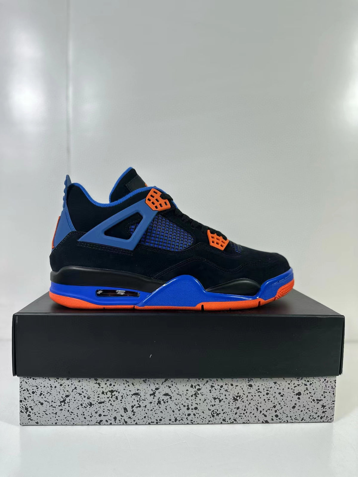 Side view of a black Air Jordan 4 sneaker with blue structural accents, orange eyelets and orange outsole details.
