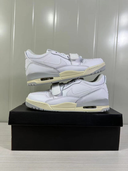 Pair of white low-top sneakers stacked on a black box, showing side profiles and cream midsole accents.