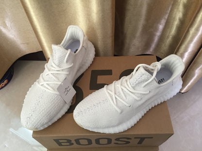 Three-quarter view of the white sneakers on a shoebox; a YEEZY inner label is visible on one shoe.