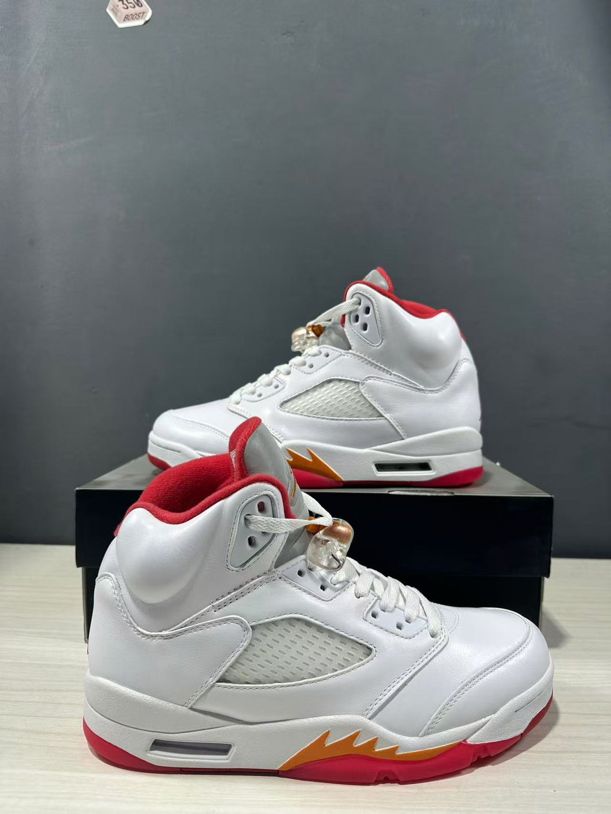 Two white high-top sneakers shown from side angles, highlighting padded collars, perforated panels and red-orange outsole details.
