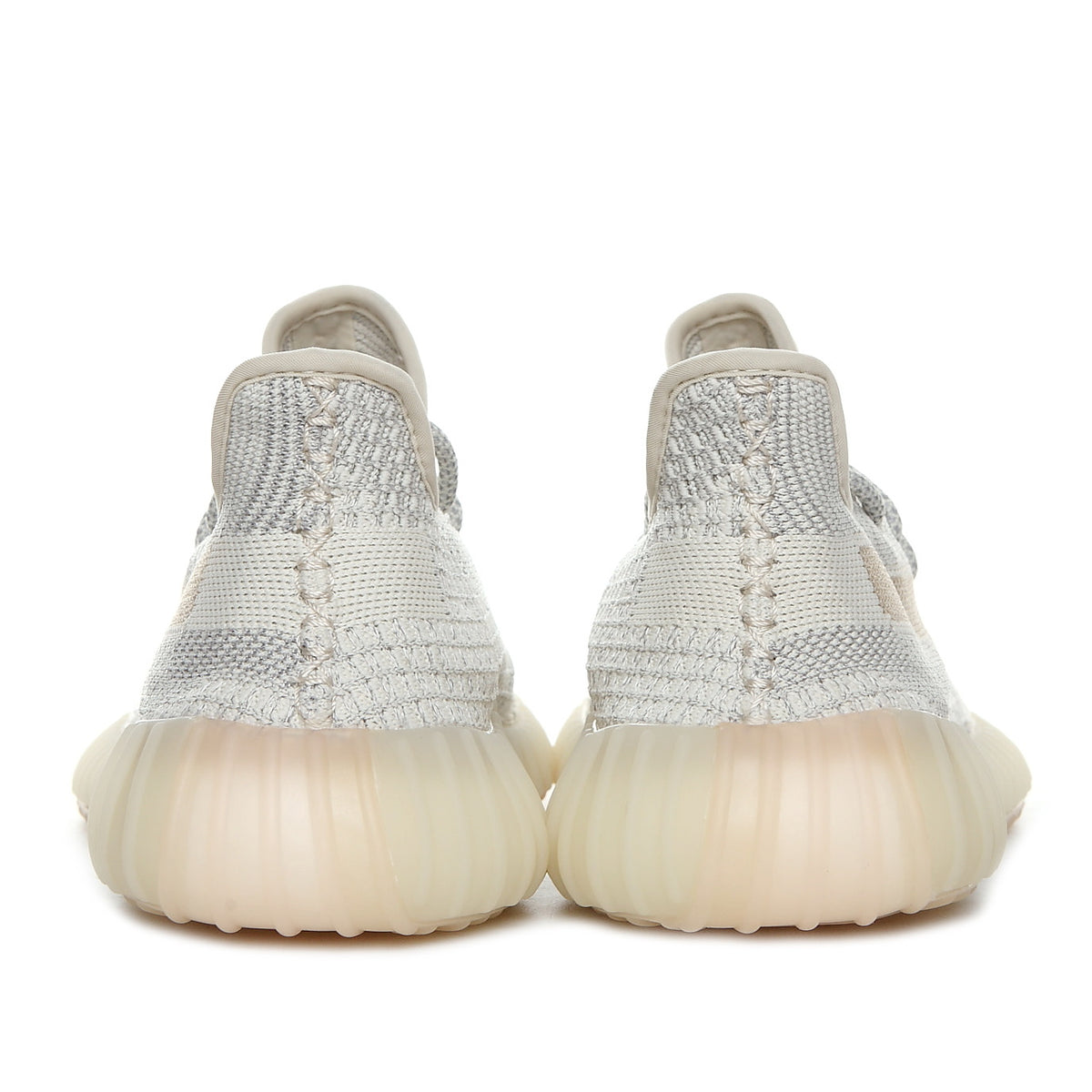 Rear view of a pair of cream and gray knit sneakers with translucent ribbed soles.