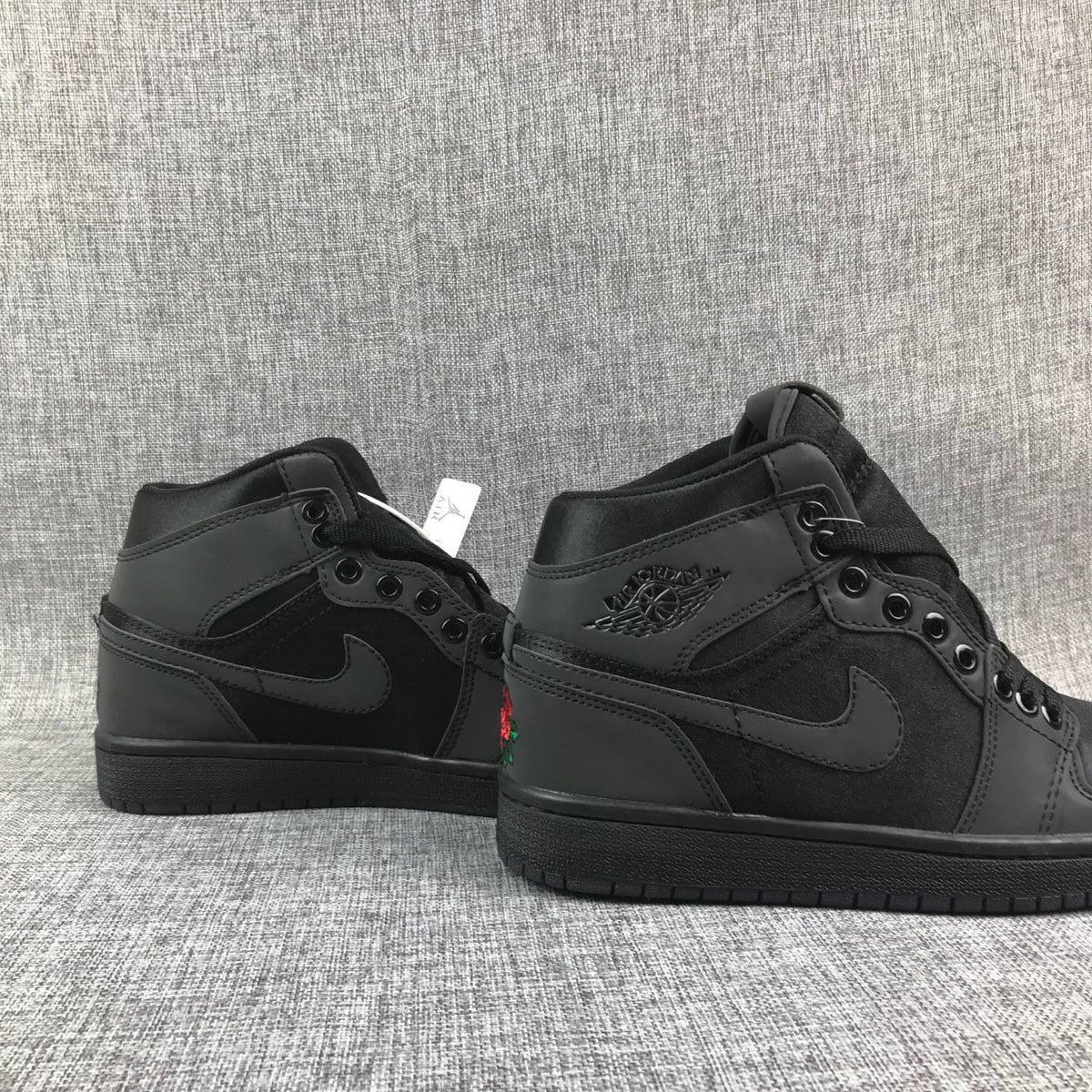 Pair of black high-top sneakers shown from the rear-side angle with rose embroidery partially visible.
