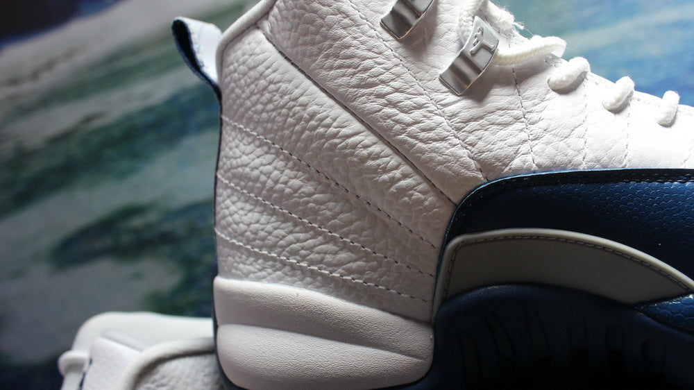 Side close-up showing the textured white upper, metal lace hardware, and navy overlay.