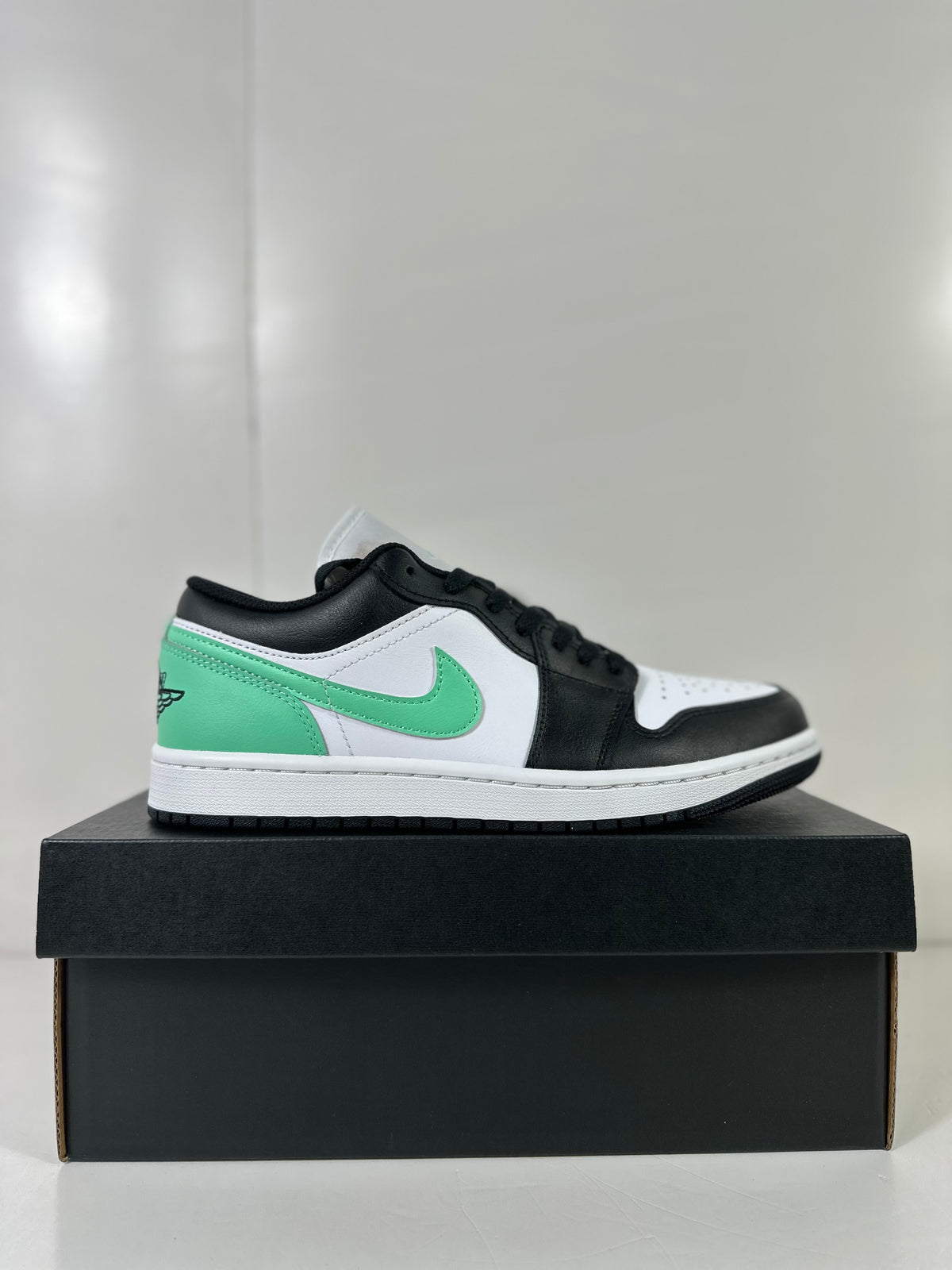 Side profile of a white, green, and black Jordan Air Jordan 1 Low sneaker displayed on a black shoebox.