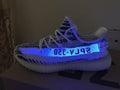 Side profile under blue light showing the patterned knit upper, side lettering, and translucent sole.