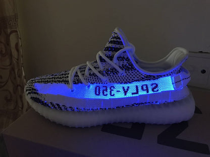 Side profile under blue light showing the patterned knit upper, side lettering, and translucent sole.