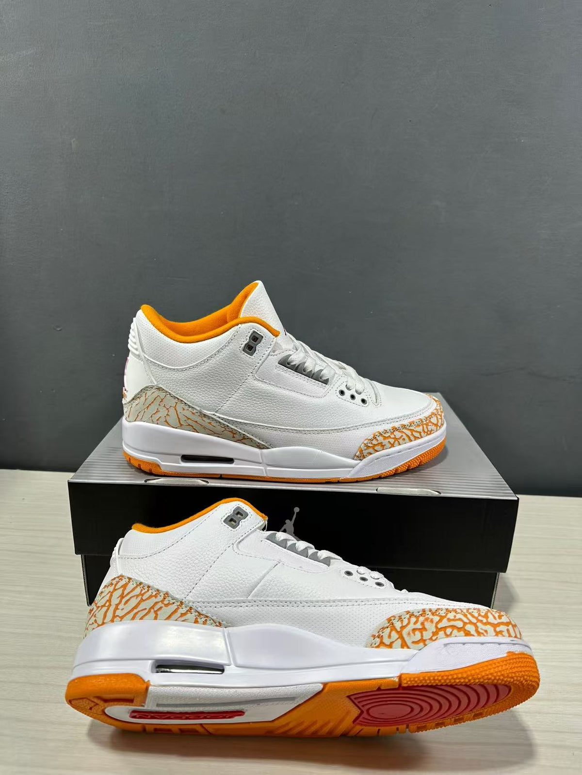 Angled product view showing the pair, white uppers, orange accents, patterned overlays and textured outsole.