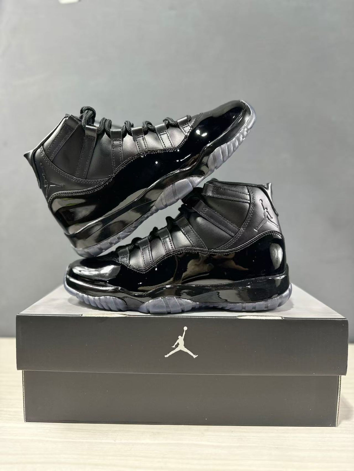 Two black high-top sneakers arranged on a Jordan shoebox, showing the side profile and translucent outsole.