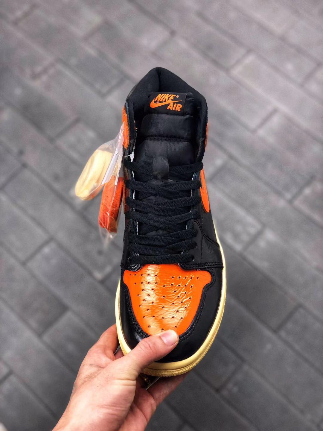 Top-down view showing black flat laces, a padded tongue, orange tongue branding, and the orange perforated toe panel.