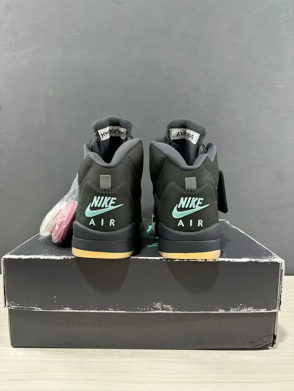 Rear view of a pair of dark green and black Jordan Air Jordan 5 sneakers showing Nike Air branding and padded collars.