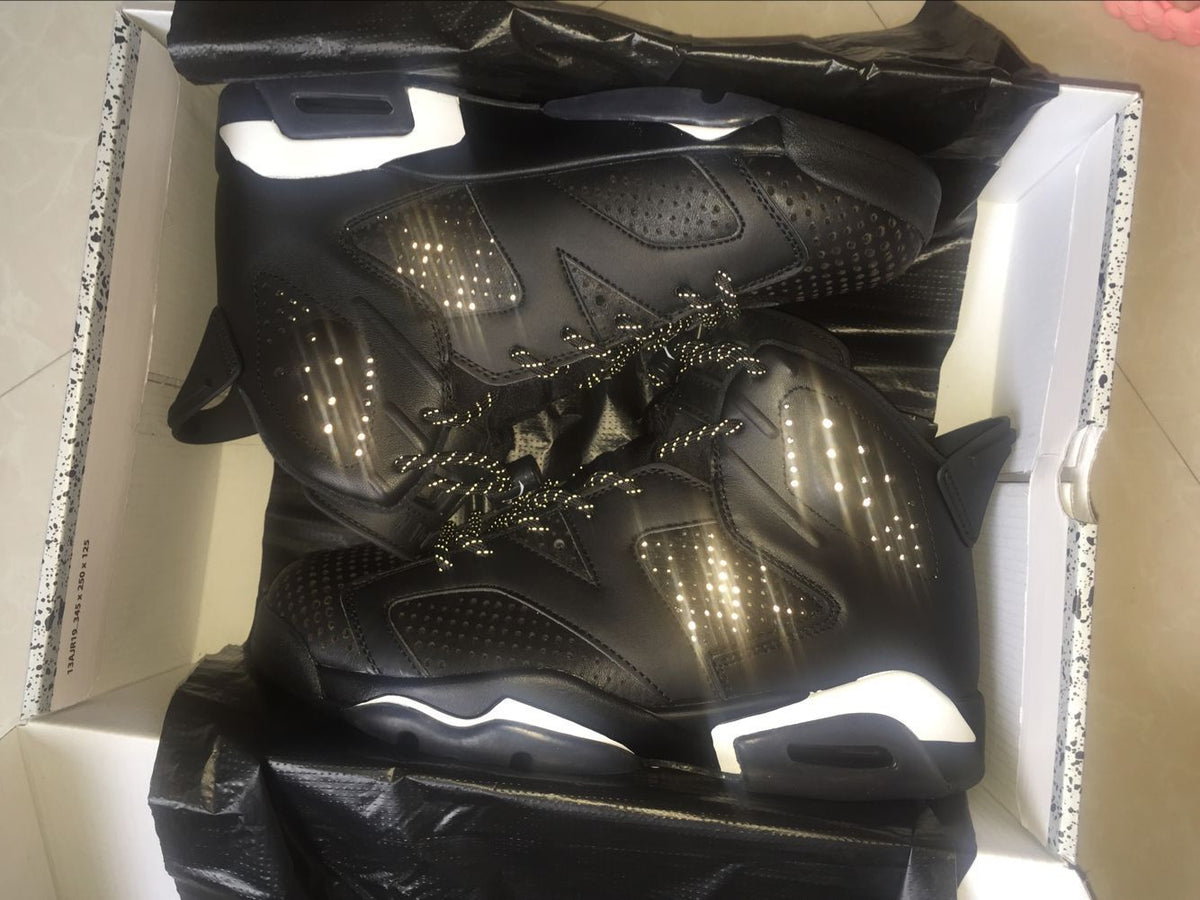 Pair of black Jordan 6 high-top sneakers photographed inside a box, showing perforated panels, reflective-style laces, and white midsole accents.