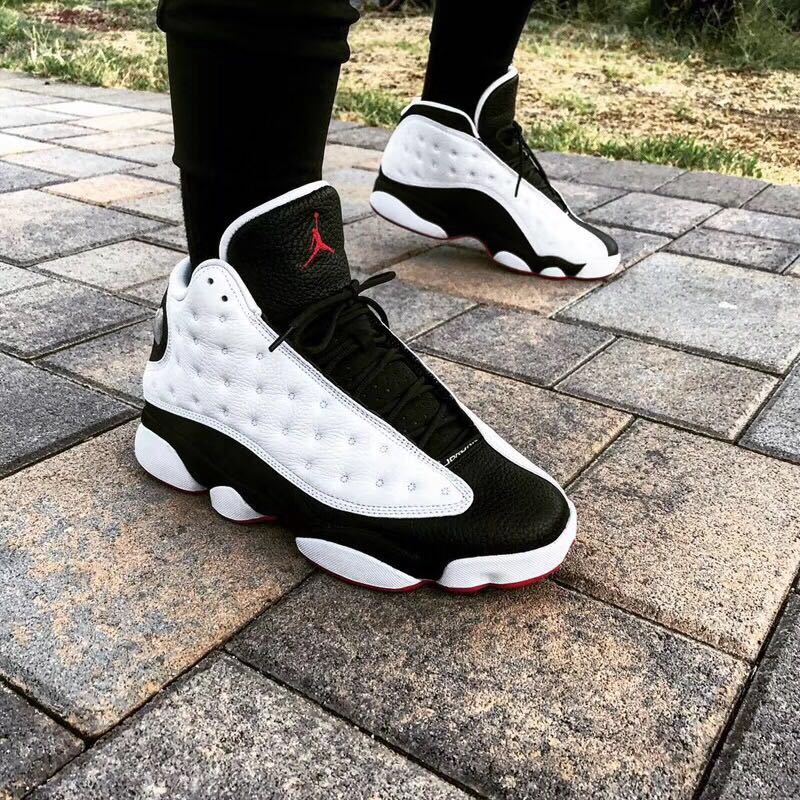 Pair of black and white high-top sneakers shown on a paved outdoor surface.
