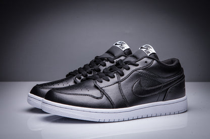 Front three-quarter view of a pair of black low-top Jordan sneakers with white soles.