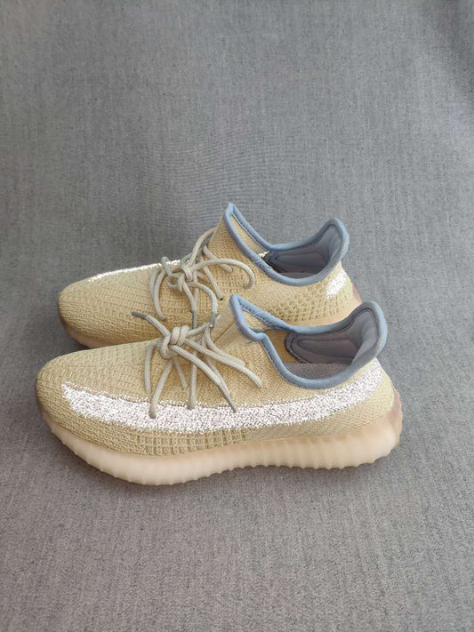 Pair of beige Yeezy 350 V2 sneakers showing the reflective side stripes and translucent soles.