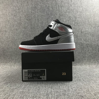 Side profile of one sneaker placed on its box; the box label shows Air Jordan 1 Mid SE GS, Black/Silver, size 6.5Y, EU 37.5 and style code 554725-057.