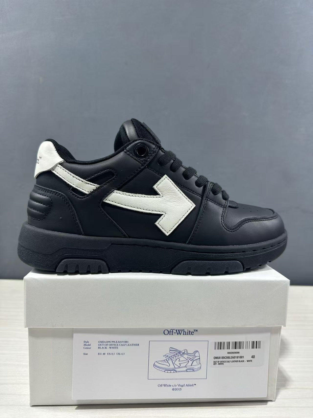 Side view of a black and white Off-White Out Of Office sneaker displayed on its product box; the box label shows the style code and a photographed EU 40 sample.