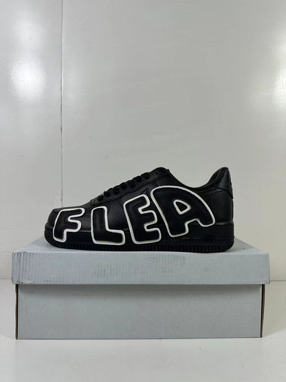 Side view of a black low-top sneaker with large outlined FLEA lettering in black and white.