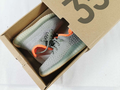 Gray and orange Yeezy 350 V2-style kids' sneakers displayed inside a cardboard shoebox.