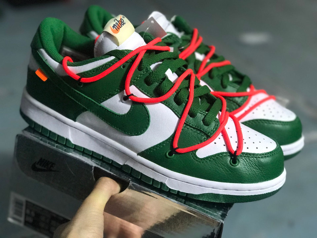 Angled front view of the white and green sneakers with red laces and perforated toe panels.
