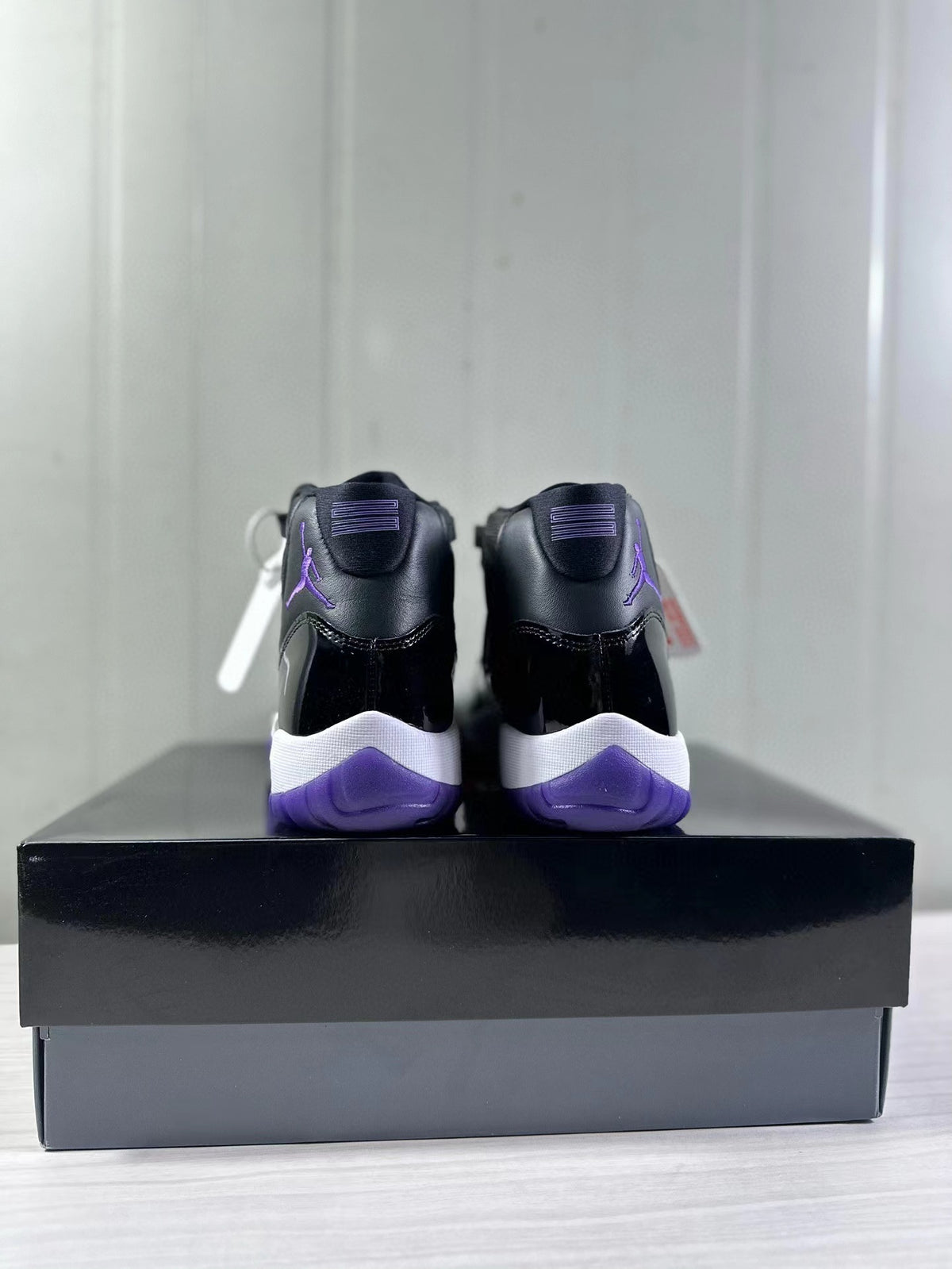 Rear view of black and purple high-top sneakers displayed on a black shoebox.