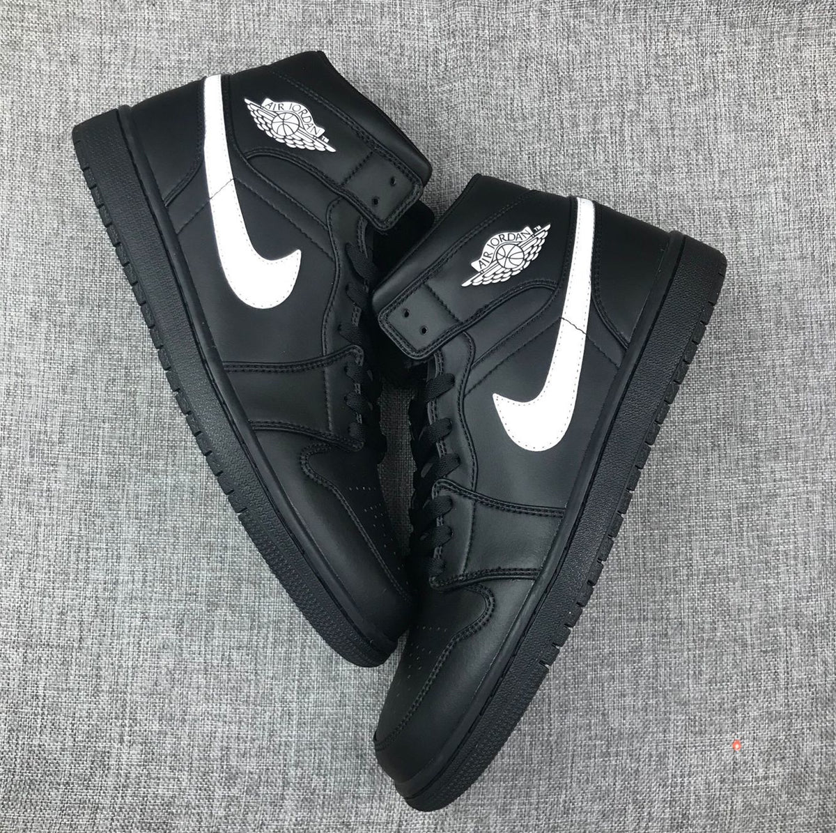 Two black and white mid-top sneakers arranged diagonally to show their side profiles and toe boxes.
