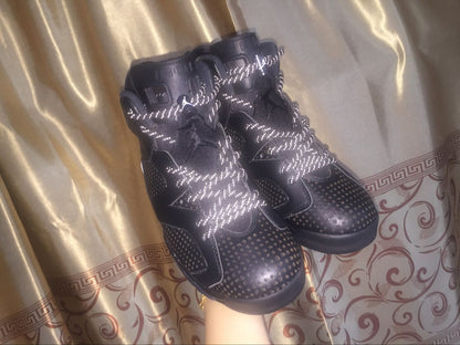 Pair of black sneakers displayed against a patterned curtain, with reflective-style laces catching the light.
