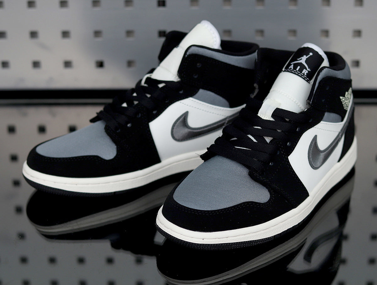 Pair of black, white and grey mid-top Jordan sneakers shown from the front three-quarter angle.