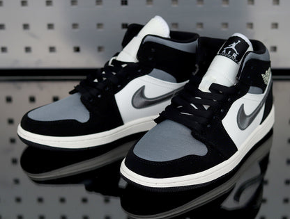 Pair of black, white and grey mid-top Jordan sneakers shown from the front three-quarter angle.