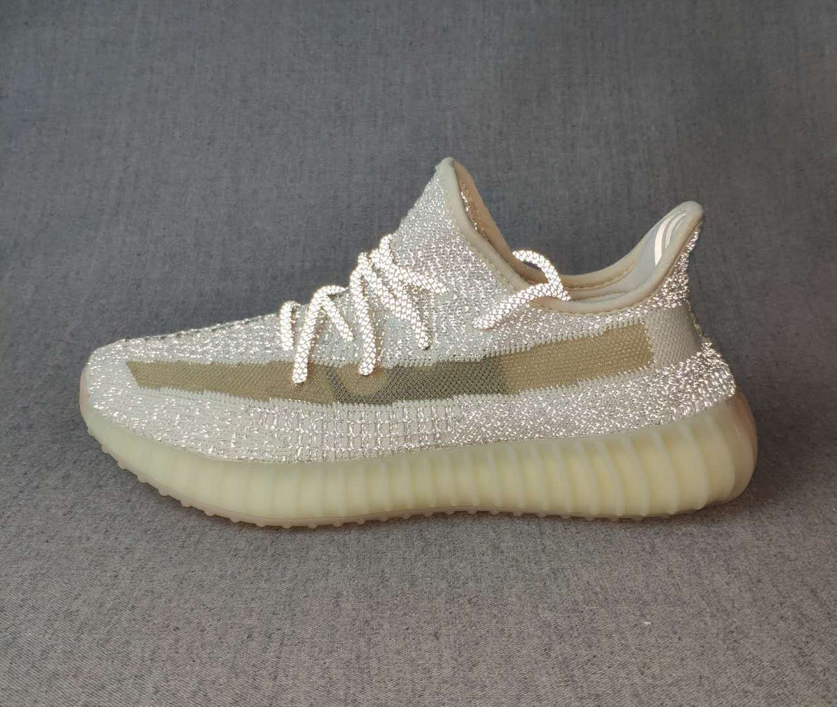Side profile of a silver-toned low-top sneaker with an olive stripe and translucent cream-colored outsole.