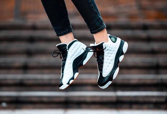 Lifestyle view of black and white Air Jordan 13 sneakers being worn on outdoor steps.