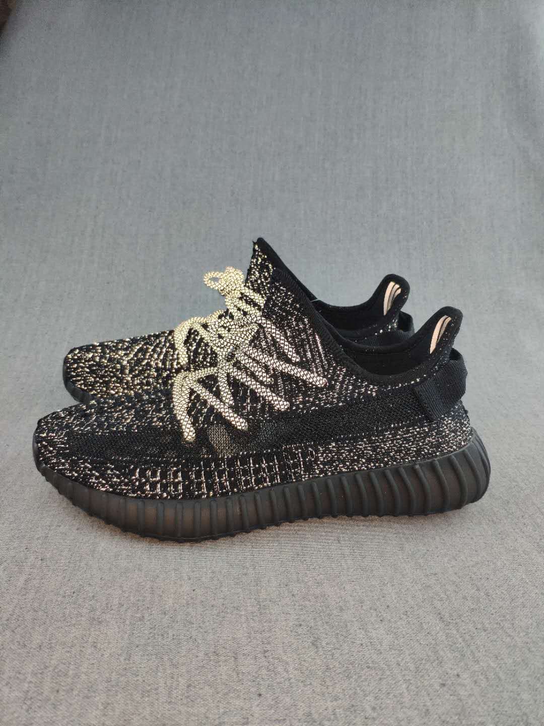 Side view of black 350 V2-style sneakers showing the textured upper, contrasting laces, ribbed outsole, and rear pull tabs.