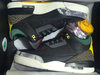 Pair of black low-top sneakers in a box, with contrasting patterned panels and an extra yellow lace set.