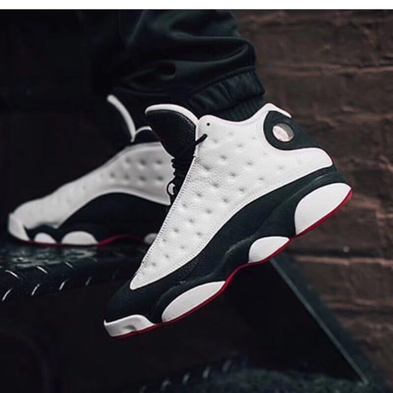 Air Jordan 13 sneakers displayed at an angle, showing the black and white color blocking and red outsole.