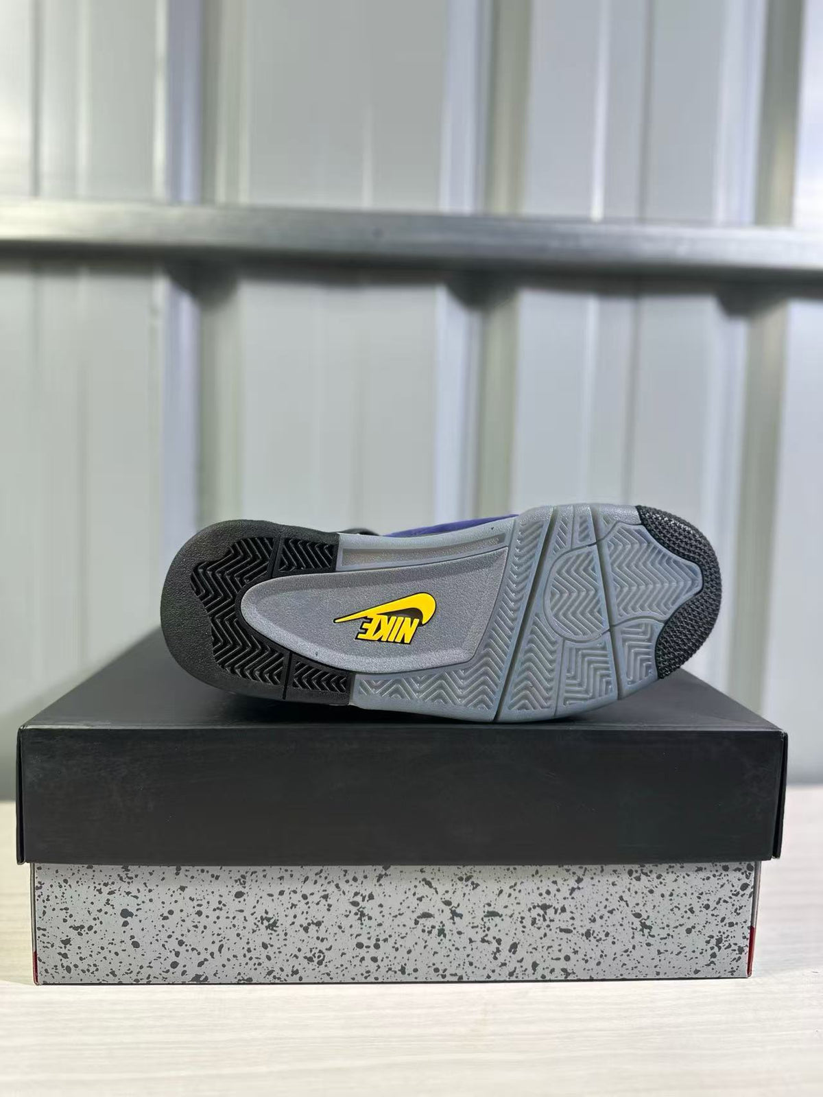 Outsole view of a Jordan Air Jordan 4 sneaker showing grey and black patterned traction sections with a yellow logo.