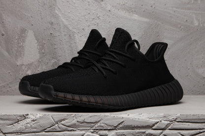 Front three-quarter view of black low-top knit-style sneakers with matching laces.
