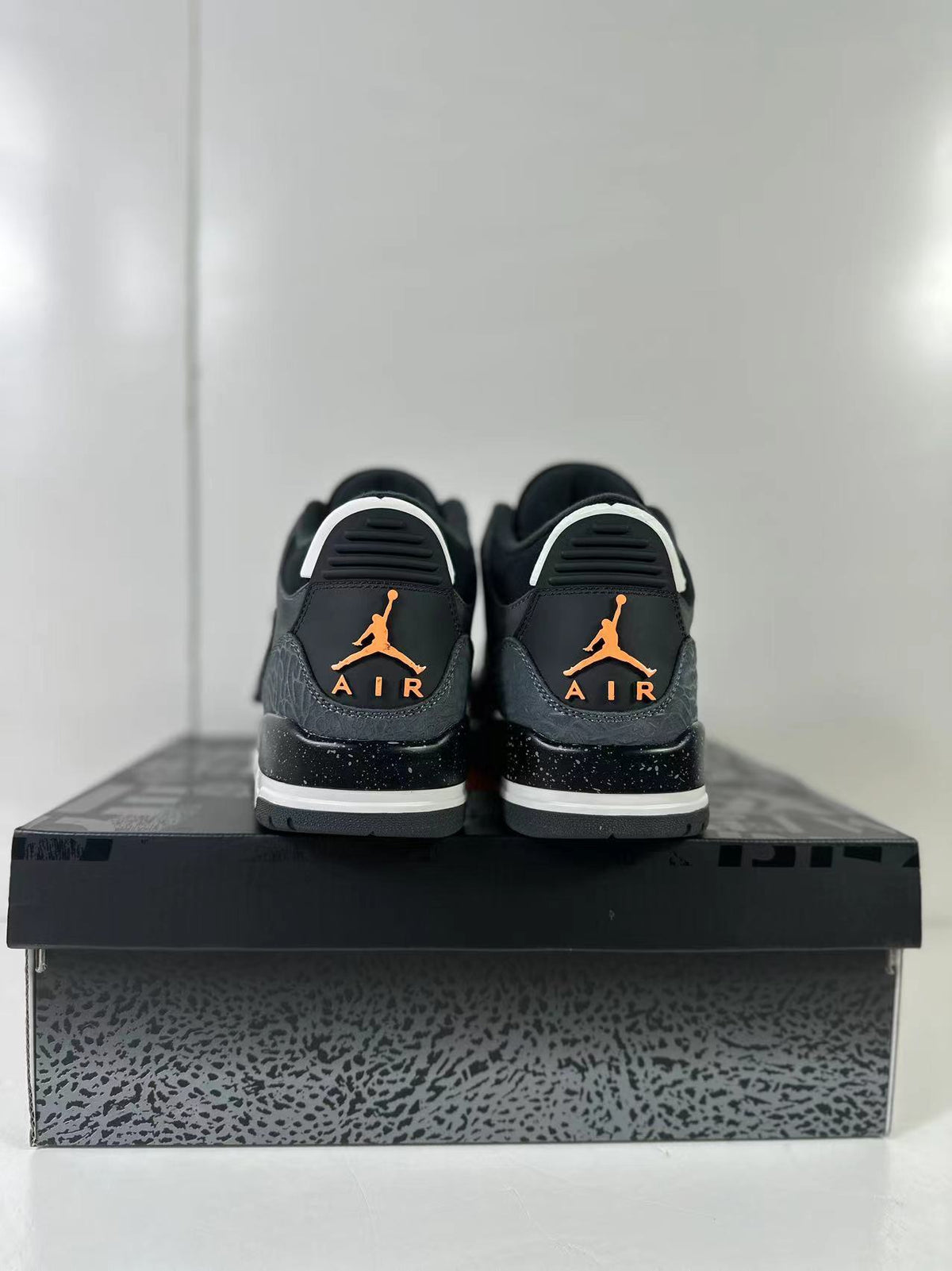 Rear view of the pair showing orange Jumpman and AIR branding, black-speckled midsoles, and elephant-print heel panels.