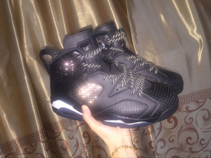 Pair of black high-top sneakers held against a curtain, showing reflective-style laces and side perforations.
