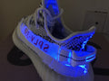 Rear-quarter view under blue light showing the heel strap, side text, and illuminated outsole.